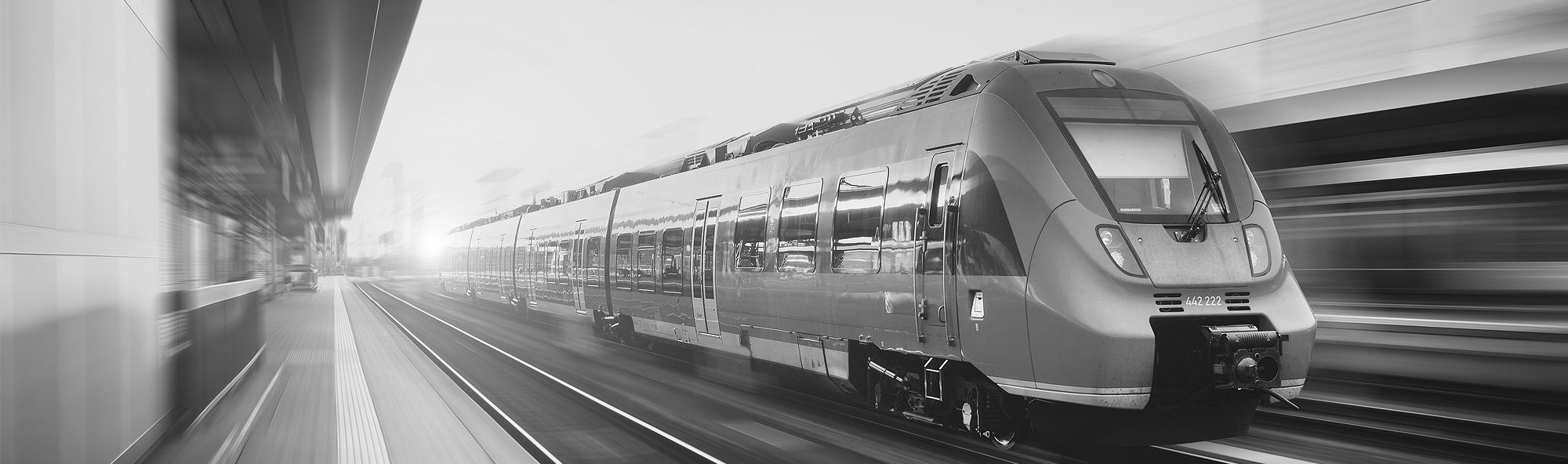 Black-and-white photograph of a train travelling past a platform
